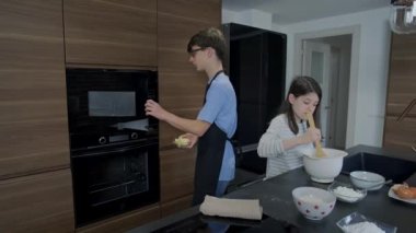 Ergen kardeşler birlikte kek pişiriyor, erkek kardeş fırını işletiyor kız kardeş mutfak kâsesinde malzemeleri karıştırıyor, aile bağlarını paylaşıyor ve yemek pişirme becerilerini öğreniyor.