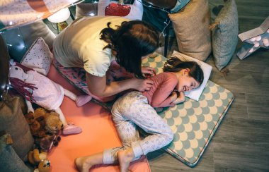 Kadın, gülümseyen genç bir kızı uyandırıp evdeki sıcak paspasların üzerinde uyuyor. Anne ve mutlu kız birlikte eğlenirken oynaşıyor ve gıdıklanıyor. Tek ebeveynli aile eğlence zamanı konsepti.