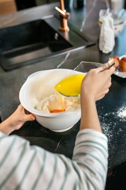 Modern bir mutfakta kek pişirmek için un ve yumurtalara erimiş tereyağı ekleyen tanınmamış genç kıza yakın durun. Evde parti için bayram tatlısı yapmak için kadın yemek pişirme becerileri..