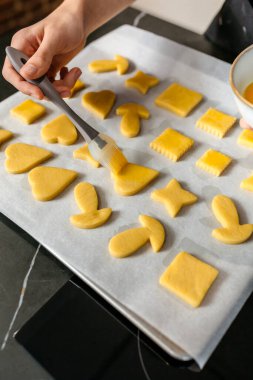 Pasta şefinin tanınmayan elleri yumurta sarısını ince ince fırçalayarak pişirme tepsisine yerleştirilmiş çiğ kurabiyeleri ustalıkla fırında pişirmeye hazırlıyor..