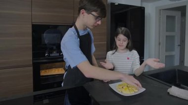 Mutfakta gülerken taze pişmiş kurabiye kızkardeşini uzatan mutlu genç erkek kardeş kardeş kardeş bağı ve şefkat dolu sıcak bir anı paylaşıyor. Aile evde yemek yaparken eğleniyor..