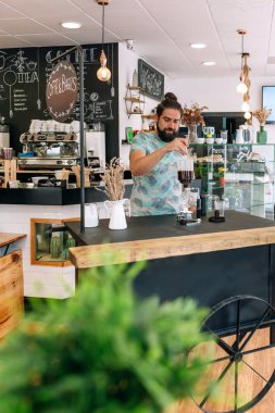Barista modern kafede Japon sifon kahve makinesiyle özel bir kahve hazırlıyor. Süslü dekorlar ve karatahta menüleriyle çevrili rahat bir ortam yaratıyor..