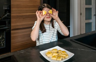 Mutfakta eğlenen genç bir kız, iki kalp şeklinde kurabiyeyi gözünün üstünde tutuyor, oyunculuğu ve zevki ifade ediyor. Küçük mutlu kız gözlerini bisküvilerle kapatırken kameraya bakıyor..