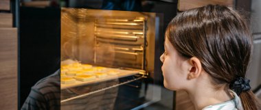 Kurabiyeleri fırında pişiren, hazır olmalarını bekleyen, kokunun tadını çıkaran ve lezzetli bir tat almayı bekleyen kız pankartı. Boş zaman konseptinde yemek pişirmek. Sol kopyalama alanı kullanılabilir.