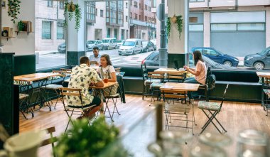 Müşteriler kahveyi seviyorlar ve parlak, davetkar bir kafede dizüstü bilgisayarlarla çalışıyorlar, modern kafe kültürünün ve şehir yaşamının özünü canlı ve sosyal bir atmosferde yakalıyorlar.