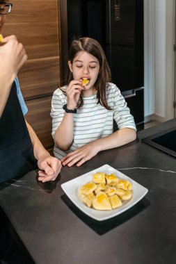 Mutlu genç kız kardeş ve erkek kardeşi modern bir mutfakta taze pişmiş kurabiyeleri tadıyorlar, emeklerinin meyvelerinin tadını çıkarıyorlar. İki çocuk lezzetli bisküviler yiyor..