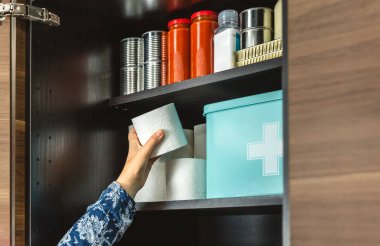 Mutfaktaki acil durum yemek kilerine tuvalet kağıdı doldurup potansiyel felaketlere karşı hazırlanan tanınmamış kadın elini kapatın. Uyanık, öngörülü ve kendi kendine yeten. 72 saat hayatta kalma kiti