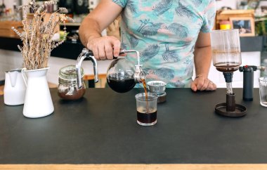 Tanınmayan barmen Japon sifon kahve makinesinden bardağa ustalıkla kahve doldurarak özel kahve hazırlama sanatını sergiliyor. Boşluğu resmin altına kopyala.