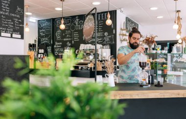 Barista modern kafede Japon sifon kahve makinesiyle özel bir kahve hazırlıyor. Süslü dekorlar ve karatahta menüleriyle çevrili rahat bir ortam yaratıyor..