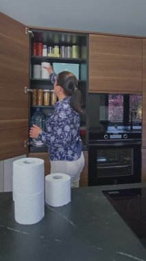 Mutfaktaki acil durum yemek kilerine tuvalet kağıdı dolduran kadın potansiyel felaketlere hazırlanıyor. Uyarı, öngörü ve kendi kendine yetme stratejisi. 72 saat hayatta kalma kiti.