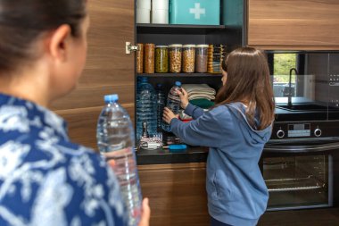 Savaş ya da doğal afetler için mutfak kilerinde yiyecek ve ilk yardım çantasıyla su şişelerini saklayan bir kız. Aile, öngörü ve kendi kendine yetme stratejisinin bir parçası olarak 72 saatlik hayatta kalma kiti hazırlıyor..