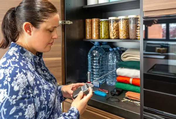 Kadın acil durum çantasının yanındaki bataryaları kontrol ediyor. Kilerdeki dolapta yiyecek, su, giyecek ve malzeme de dahil. Kadın 72 saat boyunca doğal afet ve elektrik kesintisi için hayatta kalma kiti hazırlıyor.
