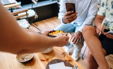 Mango, muz, ahududu, tahıl gevreği ve müsli ile yapılmış sağlıklı kahvaltı kâsesini yemek pişirme yüksek sınıfında akıllı telefonlarla fotoğraf çeken yemek blogcularına ve nüfuzlu kişilere gösteren tanınmamış bir şef..