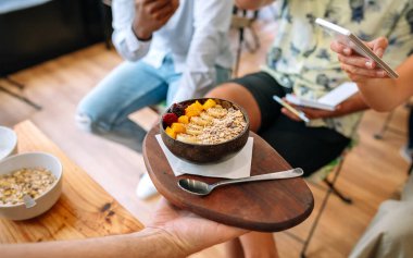 Yemek blogcularına ve nüfuzlu kişilere mango, muz, ahududu, tahıl gevreği ve müsli ile yapılmış vejetaryen kahvaltı kasesini gösteren tanınmamış bir şef yemek pişirme yüksek sınıfında akıllı telefonlarla fotoğraf çekiyor..