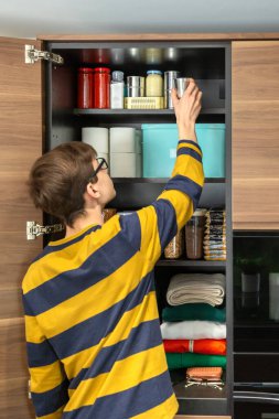 Genç adam mutfak dolabındaki acil durum çantasından konserve yiyecek alıyor. Ergen ergenler gıda kaynaklarını kontrol ediyor ve kilerde bozulmayan şeyler depoluyor, elektrik kesintisine ya da doğal afetlere hazırlanıyor..