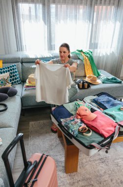 Oturma odasındaki kanepede oturan ve macera ve rahatlıkla dolu heyecanlı bir yaz tatiline hazırlanan kadın bavulunu hazırlıyor.