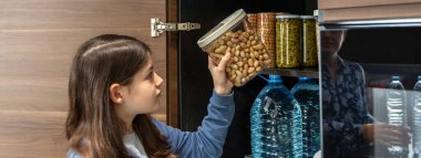 Dolapta depolanmış 72 saatlik hayatta kalma kitine fıstık ekleyen bir kız. Kadın mutfakta acil yemek kileri hazırlıyor, felaketler için. Uyarı, öngörü ve kendi kendine yetme stratejisi.