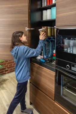 Dolapta depolanmış 72 saatlik hayatta kalma kitine fıstık ekleyen bir kız. Kadın mutfakta acil yemek kileri hazırlıyor, felaketler için. Uyarı, öngörü ve kendi kendine yetme stratejisi.