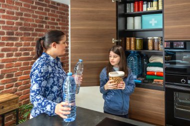 Aile 72 saatlik hayatta kalma kiti hazırlıyor. Mutfak kilerinde yiyecek ve su şişeleri savaş ya da yiyecek kıtlığı için hazır. Kadın ve kız acil durum ve kendine yetme stratejisi hazırlıyorlar..