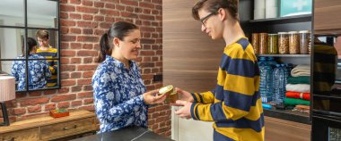 Mutfaktaki gülümseyen ergen oğluna teneke kutu yiyecek taşıyan mutlu anne pankartı. İçinde konserve yiyecekler ve bozulamaz eşyalar var. Elektrik kesintisi ya da felaket için aile malzemeleri düzenleme