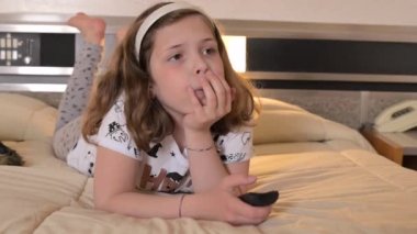 Girl with a remote control on the bed. The child watches TV in the room or in the hotel. Close-up of a child of European appearance 8 or 9 years old. High quality 4k footage