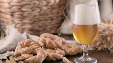 Pouring beer into the glass. Wheat spikelets with one mugs of beer on wooden background. Cold lager beer. Craft beer forms waves. Freshness and foam.Nearby are Neapolitan taralli from Italy. Ffootage