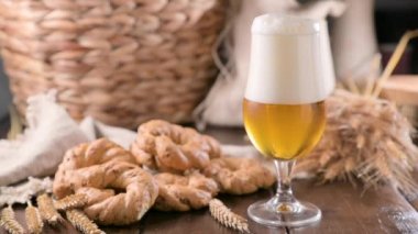 Pouring beer into the glass. Wheat spikelets with one mugs of beer on wooden background. Cold lager beer. Craft beer forms waves. Freshness and foam.Nearby are Neapolitan taralli from Italy. Ffootage