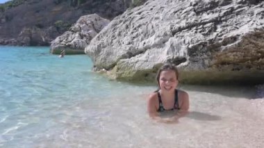 Little girl on the beach plays in the waves. Pure azure sea and sun glare. Happy moment for a child. High quality FullHD footage