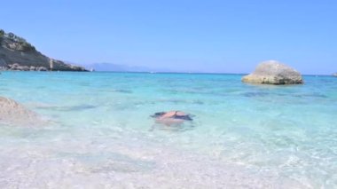 Little girl on the beach plays in the waves. Pure azure sea and sun glare. Happy moment for a child. High quality FullHD footage