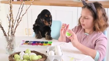 Little girl paints eggs for Easter. Child schoolboy of European appearance and Easter eggs, decor on the table. Light interior and natural shots. High quality 4k footage