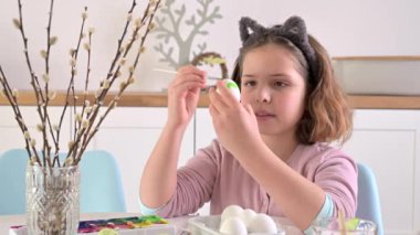 Little girl paints eggs for Easter. Child schoolboy of European appearance and Easter eggs, decor on the table. Light interior and natural shots. High quality 4k footage