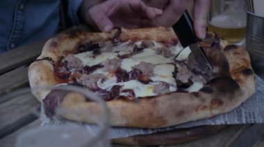 Salsiccia 'lı bir restoranda pizza. Peynirli, etli ve marullu Napoli pizzası. Eller pizzayı dilimlere ayırıyor. Yüksek kalite 4k görüntü