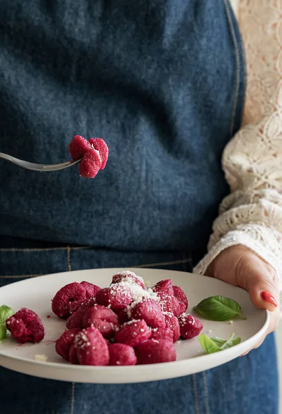 Italian gnocchi beetroot . Traditional Italian food in a bowl is held by a woman in an apron. Handmade potato balls with parmesan and beets. Food for vegetarians and lovers of Italian typical cuisine