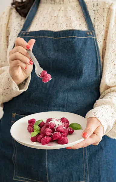 Italian gnocchi beetroot . Traditional Italian food in a bowl is held by a woman in an apron. Handmade potato balls with parmesan and beets. Food for vegetarians and lovers of Italian typical cuisine