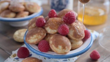  Altın Hollanda Poffertjes şuruplu ve böğürtlenli. Lezzetli geleneksel mini krepler tabakta. Bal, küçük kreplere mavi desenli beyaz bir tabakta dökülür.