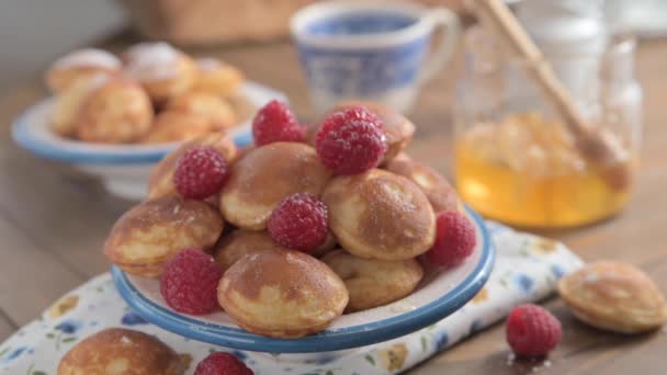 シロップとベリーが付いている黄金のオランダのポファルトゥーセのクローズアップ プレートの上の美味しい伝統的なミニパンケーキ 青いパターンが付いている白い版のミニパンケーキの蜂蜜のポーズ — ストック動画