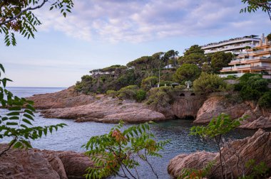 Rocky Shoreline ve Villas Akdeniz manzaralı İspanyol Sahil Manzarası. Kayalık kıyılar, geleneksel Akdeniz villaları ve açık mavi gökyüzüne karşı yemyeşil yemyeşil. 