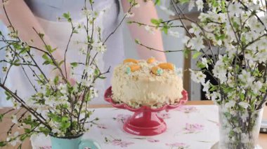 Pasta pastası pastel yumurta ve çiçeklerle süslenmiş, kırmızı bir standa konmuş. Çiçek açan dalları olan narin ve şenlikli bir sahne. Paskalya, kutlamalar ve mevsimlik neşe için mükemmel. Yüksek kalite 4k 