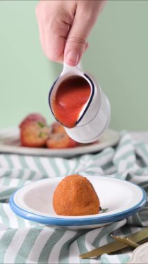 Sicilya usulü gevrek arancini 'nin üzerine acı domates sosu döküldü. Geleneksel İtalyan pirinç topları taze servis edilir. Yemek hareketi yakın plan. Yüksek kaliteli FullHD görüntüler