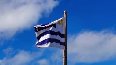 Uruguay bayrağının düşük açılı, yavaş çekim videosu zarif bir şekilde gökyüzüne karşı dalgalanıyor, Plaza Democracia, Montevideo City, Uruguay 'daki La Bandera anıtında yakalandı.