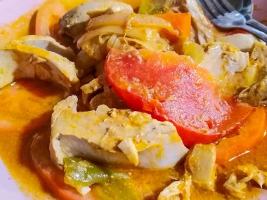 Pembe tabakta servis edilen ev yapımı balık yahnisinin orta boy ön görüntüsü, zengin, portakal suyunda kalın balık, domates, soğan ve yeşil biber dilimleri yer alıyor.. 