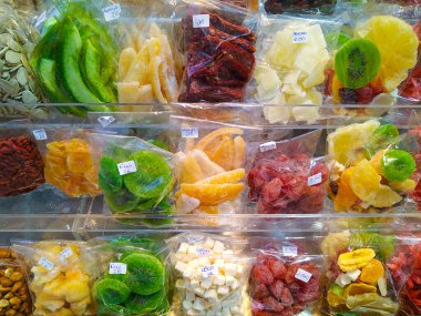 Açık plastik poşetlerde kurumuş meyvelerin yer aldığı renkli bir piyasa görüntüsünün orta açıdan çekilmiş hali. Ağırlık ve tipe göre etiketlenen bileşim, canlı ve organik bir düzende bolluk ve çeşitliliği yakalar.