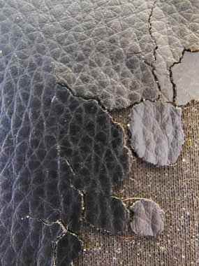 Kırık, siyah deri benzeri bir yüzeye yakın çekim. Hasarlı, sürüngen deseni yaş, çürüme ve direnç kavramlarını çağrıştırıyor..