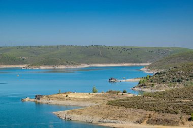 Yuvarlanan tepelerin arasında kurumuş arazi ve en az bitki örtüsü olan sakin mavi gölün göz hizasında görüntüsü..