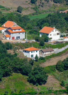 Kırmızı çatıları ve dağlık arazilerle çevrili dağınık evleri olan geleneksel kırsal bir köyün yüksek açılı manzarası.