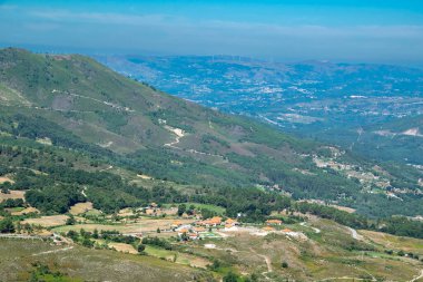 Yoğun ormanları, dağınık evleri ve bulanık mavi gökyüzünün altında dolambaçlı yolları olan engin bir dağ vadisinin yüksek açılı manzarası.