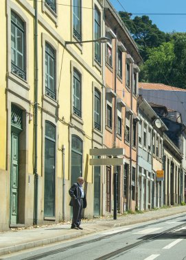 Porto, Portekiz: 12 Ağustos 2023: Porto 'da gölgeli bir cadde boyunca uzun ağaçların altında park edilmiş tarihi sarı bir tramvayın orta görüş açısı.