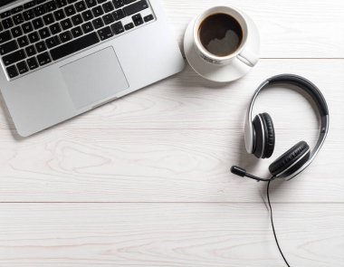 Kapalı bir dizüstü bilgisayar, kablosuz kulaklık ve kahve fincanını gösteren temiz bir masa başı fotoğrafı. 