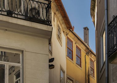 Pastel binalarla kaplı dar bir kaldırım taşının ön cephesinden çekilen hafif gün ışığı altında işlenmiş demir balkonlar.