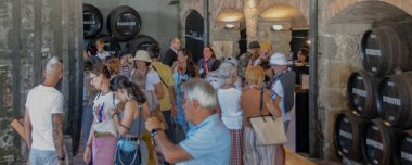 Porto, Portekiz: 12 Ağustos 2023: Turistlerin meşe fıçıları ve sıcak iç ışık altında taş duvarlarla çevrili tarihi bir mahzende porto şarabı tattıkları ön yüksek açılı orta açı fotoğraf